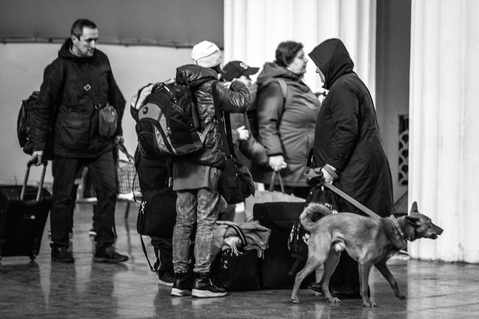 Personas con maletas y mochilas esperando durante una evacuación, en blanco y negro