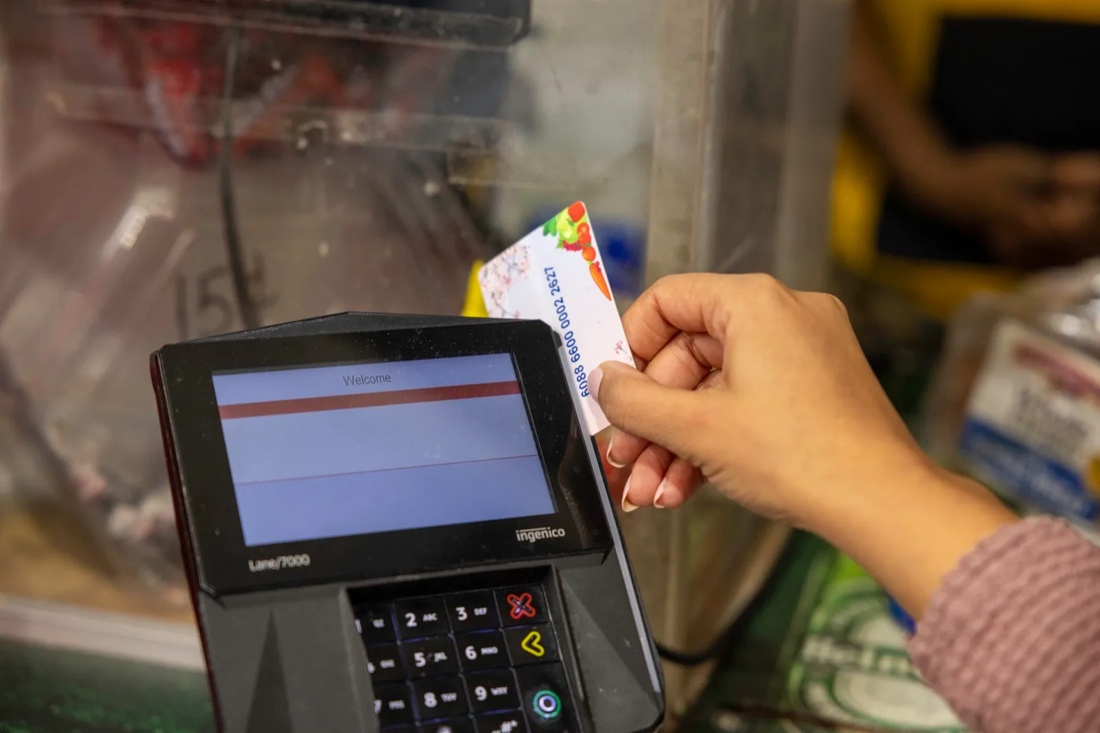 Una mano desliza una tarjeta de beneficios de alimentos en un lector de pagos de una tienda