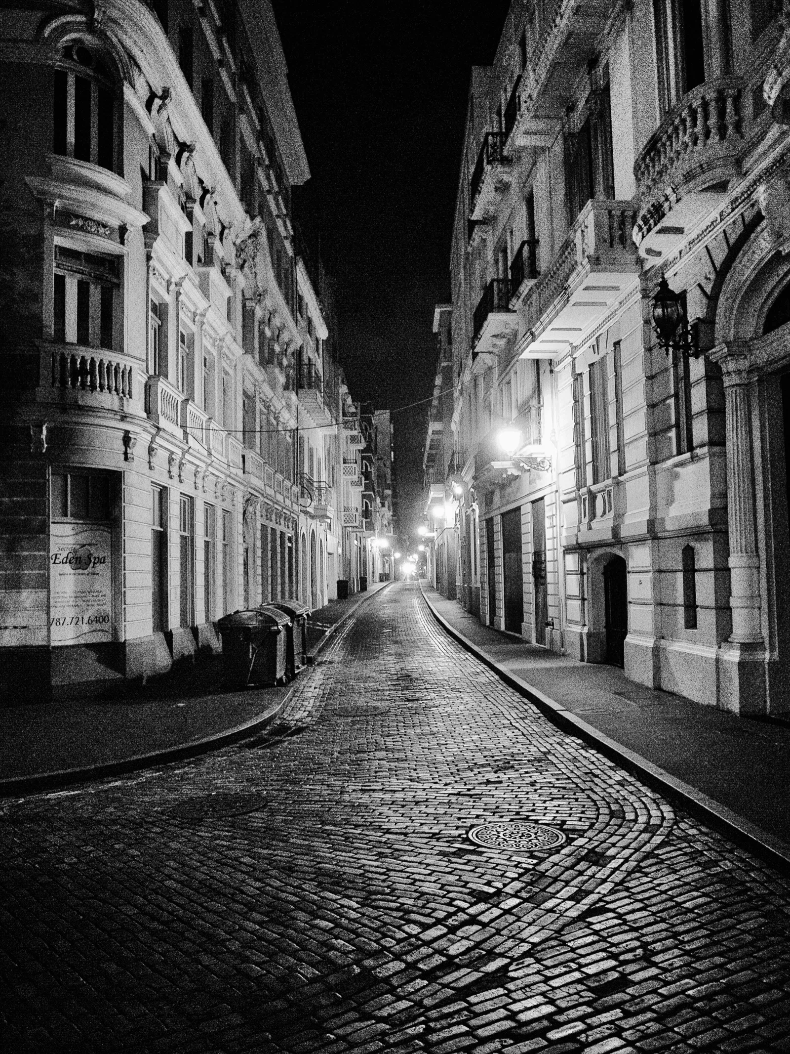 Calle empedrada del Viejo San Juan, vacía y de noche, con edificios coloniales iluminados, en blanco y negro