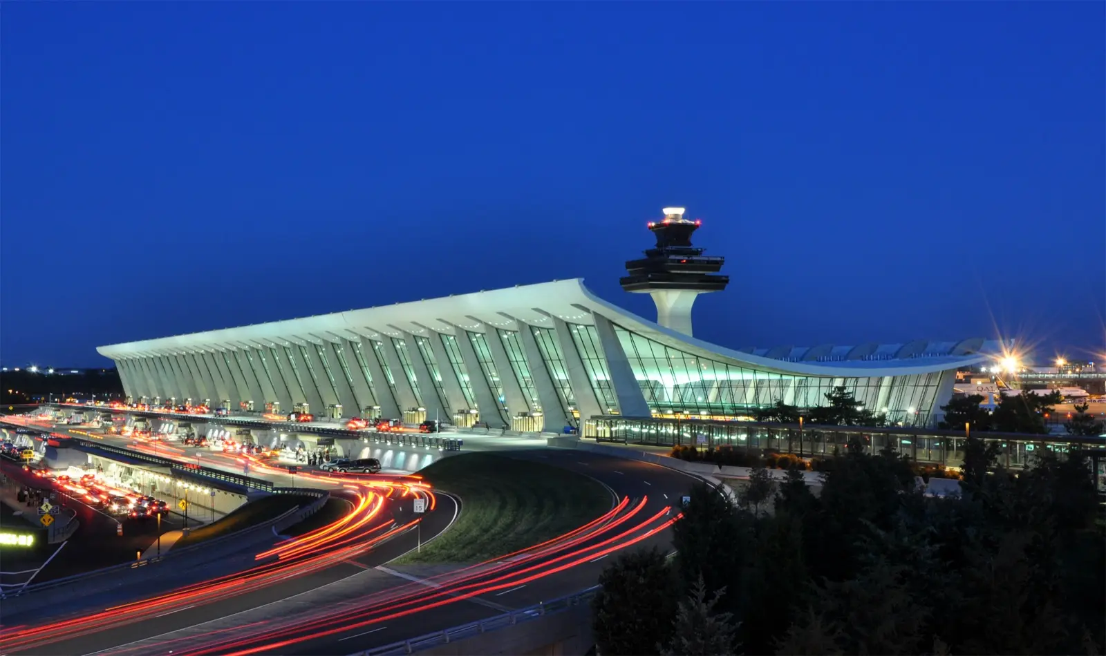 Terminal del aeropuerto internacional de Washington Dulles al anochecer, con la torre de control iluminada y estelas de luz de los carros