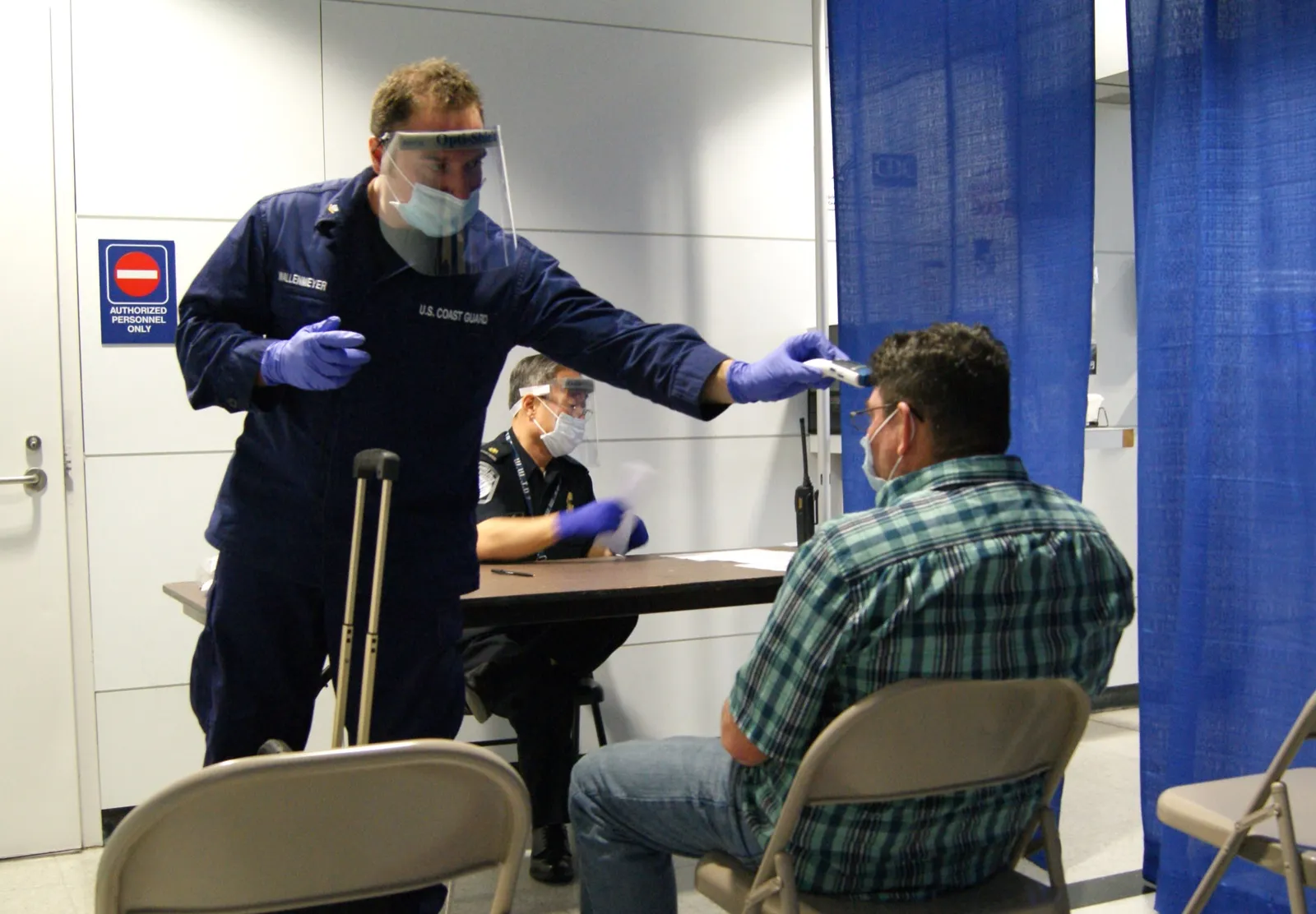 Oficial con visor y mascarilla toma la temperatura a un pasajero durante un control de ébola en un aeropuerto de Estados Unidos