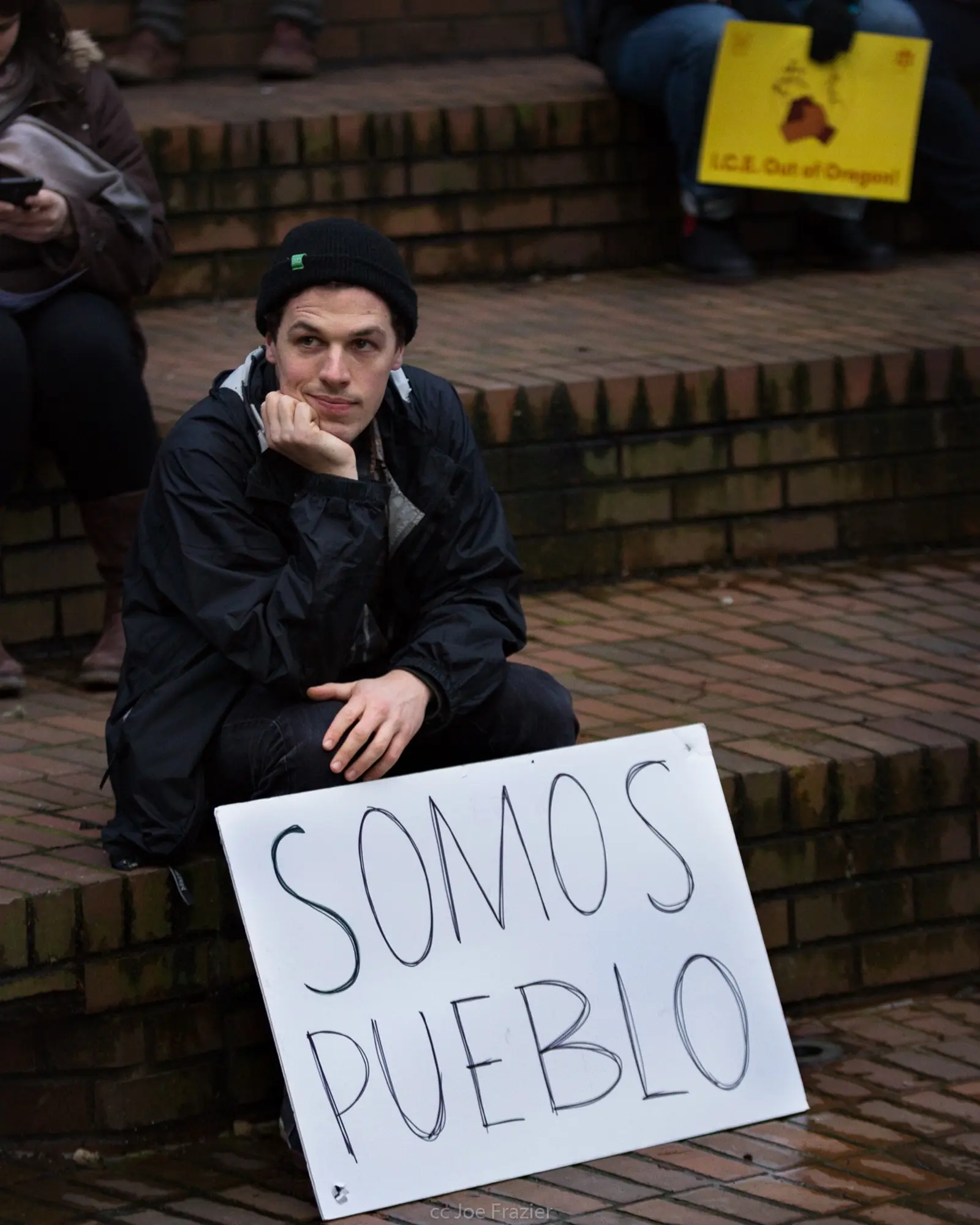 Joven sentado en unas escaleras junto a un cartel que dice «Somos pueblo» durante una manifestación en defensa del DACA