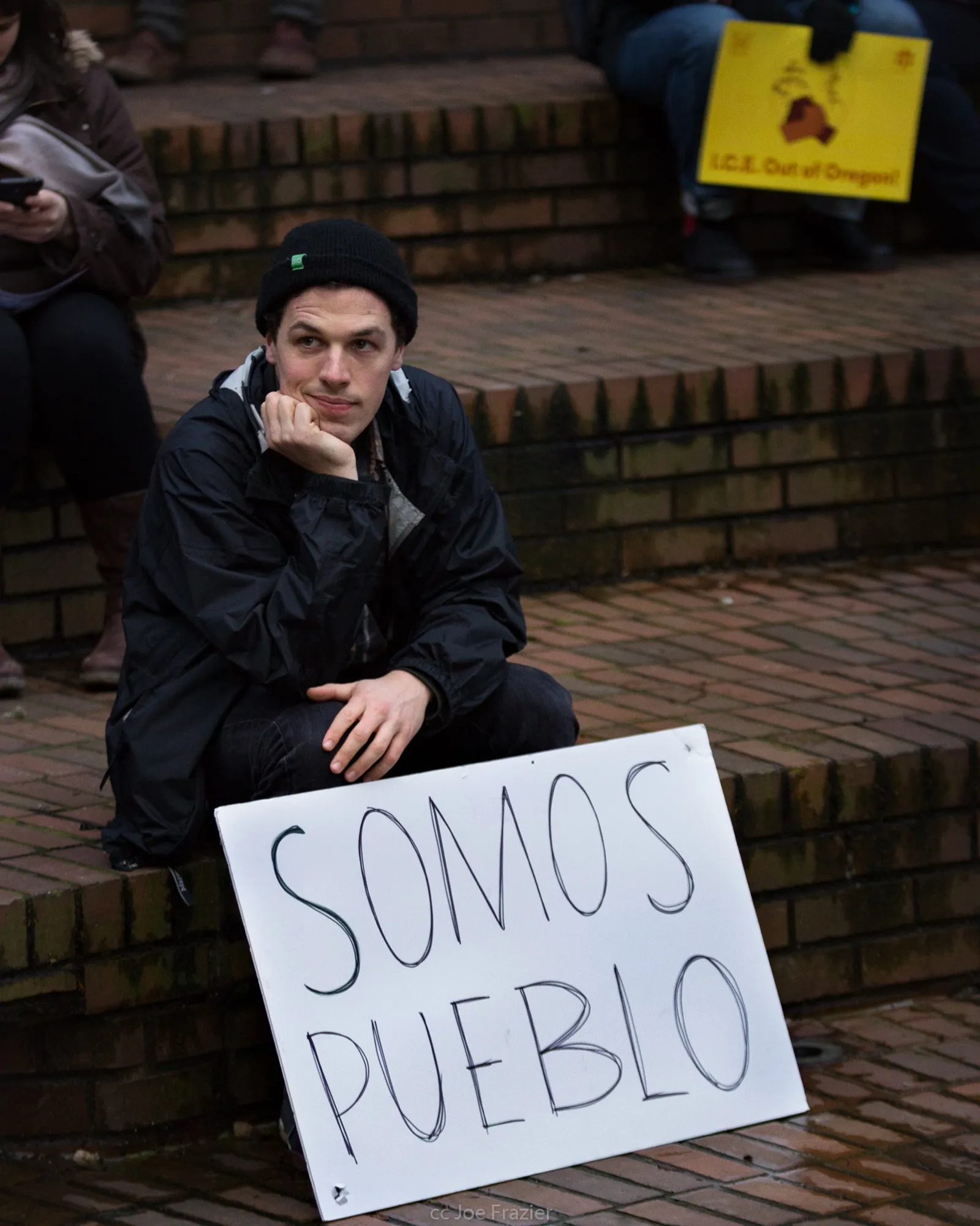 Joven sentado en unas escaleras junto a un cartel que dice «Somos pueblo» durante una manifestación en defensa del DACA