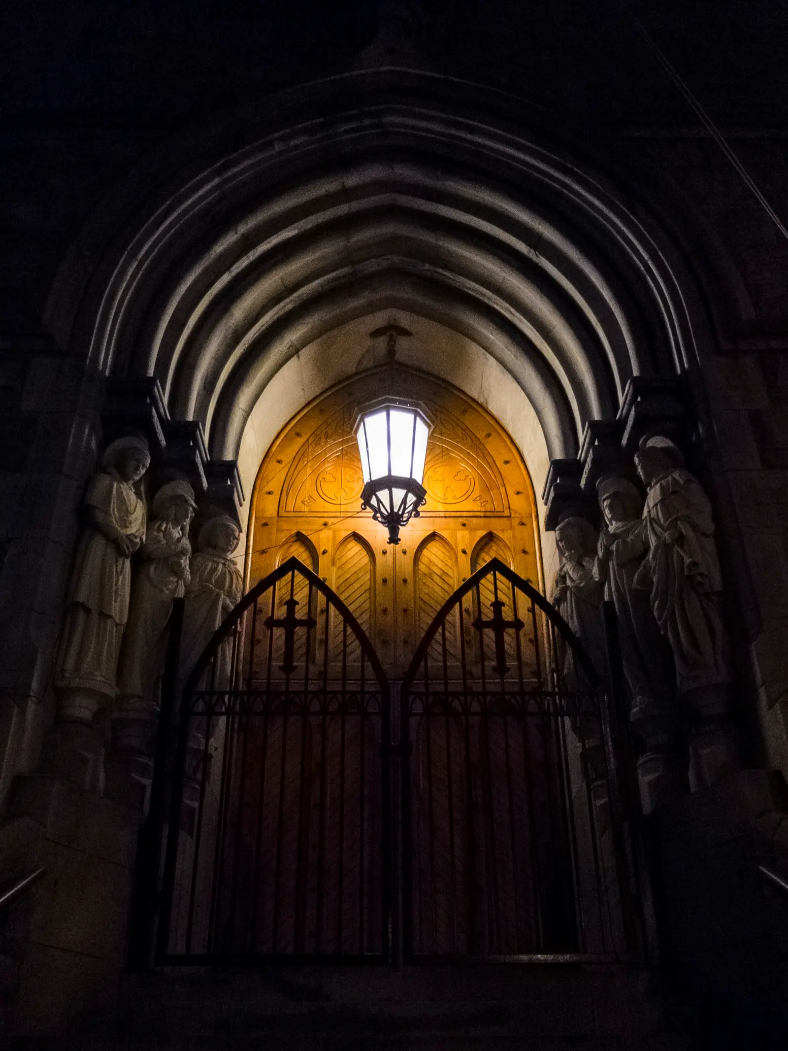 Puerta de una iglesia iluminada de noche, con un farol encendido sobre el portón