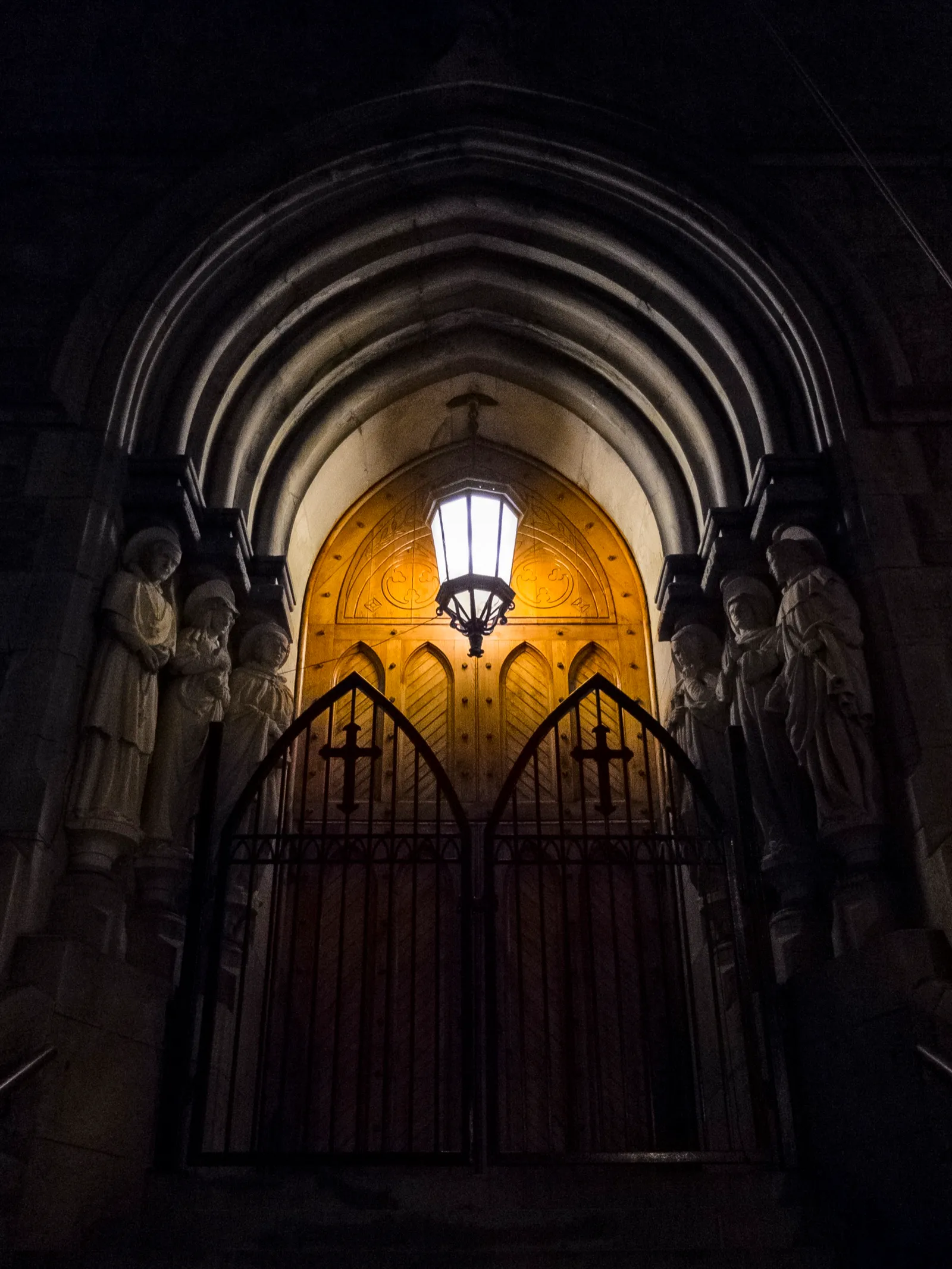 Puerta de una iglesia iluminada de noche, con un farol encendido sobre el portón