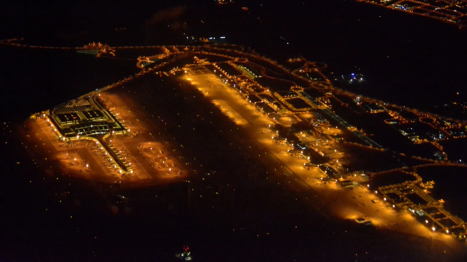 Vista aérea nocturna de un aeropuerto con las pistas y la terminal iluminadas