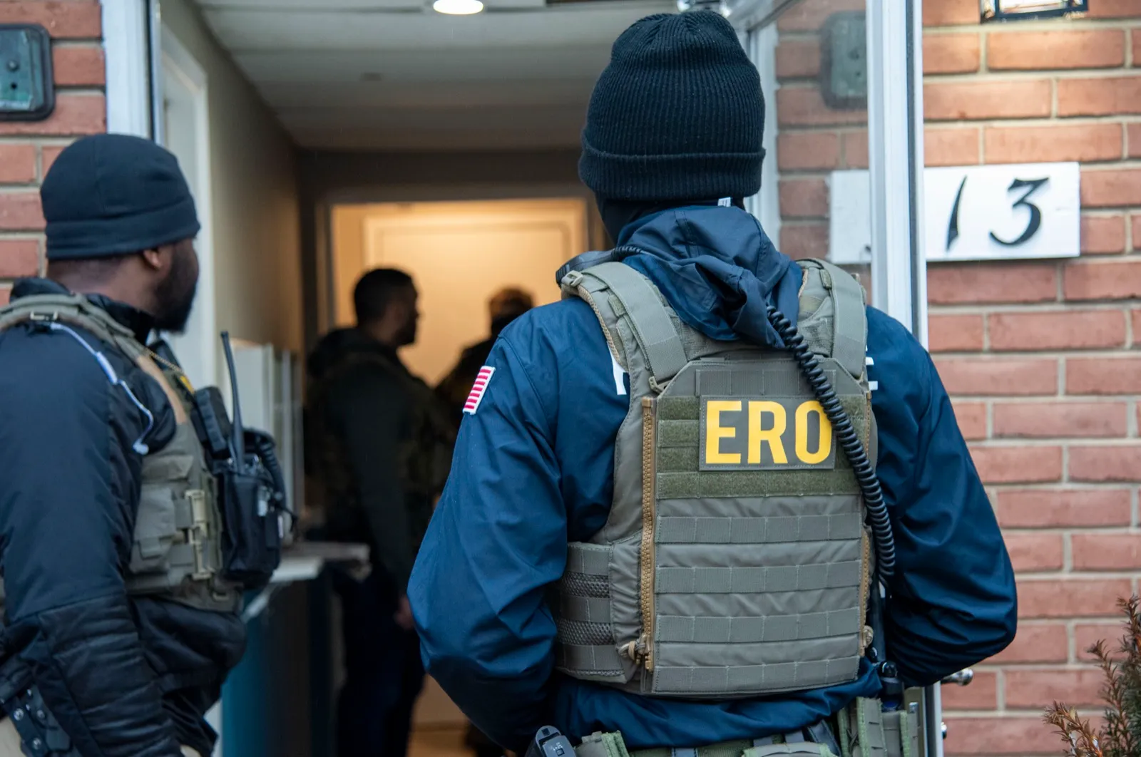 Agente de ICE de la oficina de Operaciones de Remoción (ERO), de espaldas, frente a la puerta de una vivienda