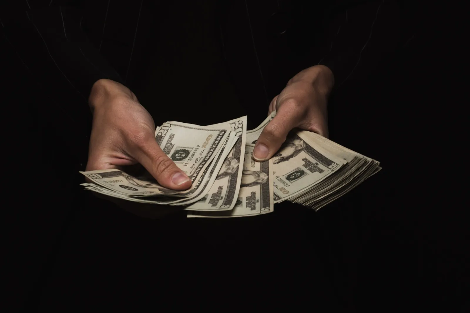 Manos contando billetes de dólar sobre un fondo oscuro