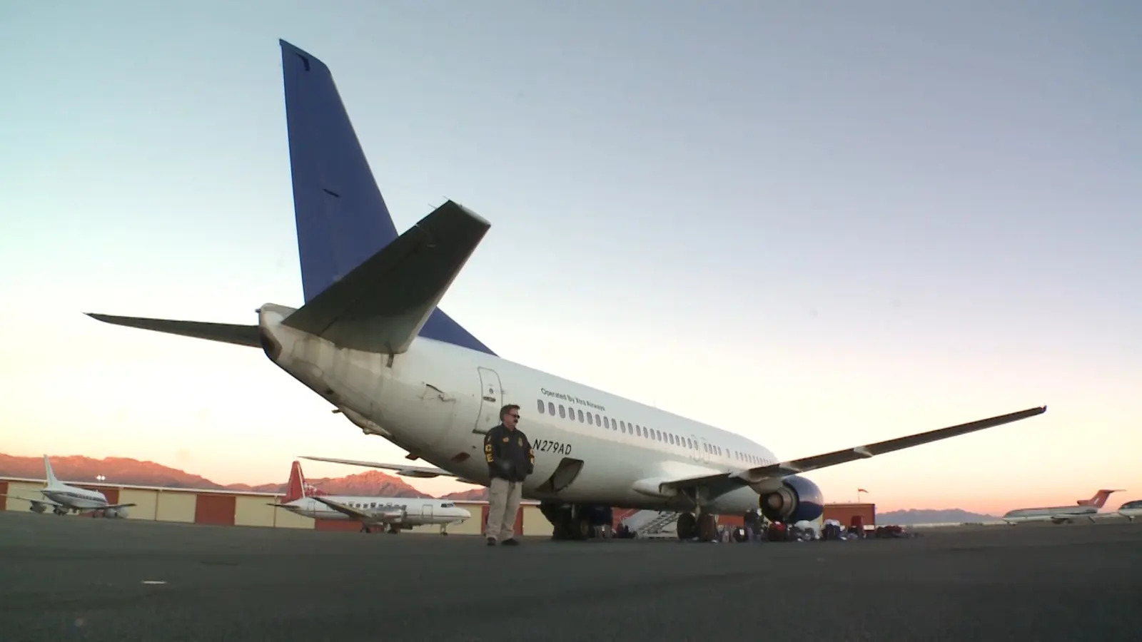 Un agente de ICE junto a un avión que se prepara para un vuelo de deportación