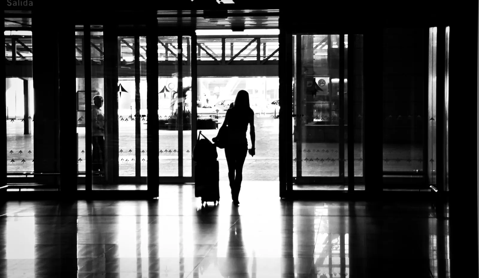 Silueta de una mujer con una maleta saliendo de un aeropuerto