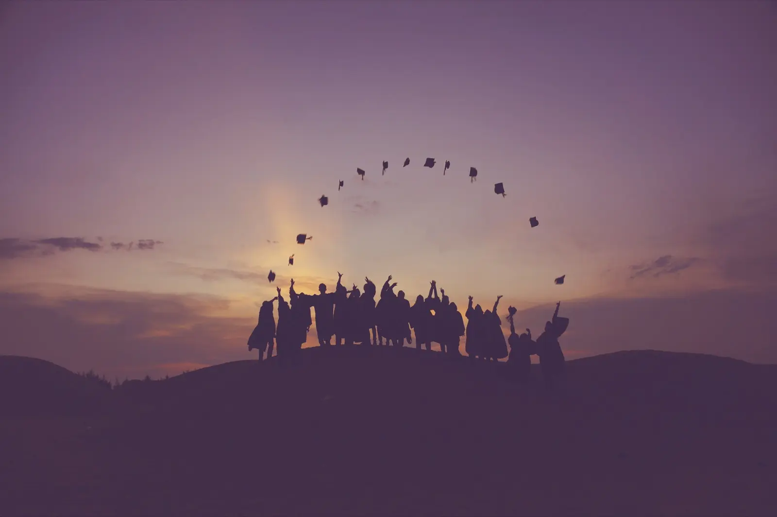 Silueta de un grupo de graduados lanzando sus birretes al aire al atardecer